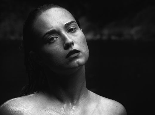 Eine nachdenklich blickende Frau mit nassen Haaren vor einem dunklen Hintergrund.