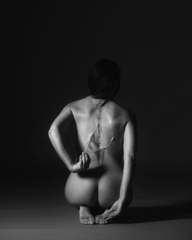 Sicht auf einen nackten Rücken einer Person, die in einem kontemplativen Moment sitzt.