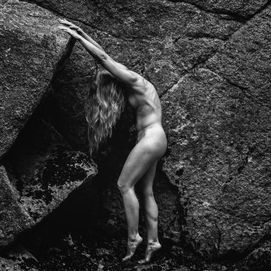 Eine nackte Person hängt an einer Felswand in einem dramatischen Schwarz-Weiß-Kontrast.